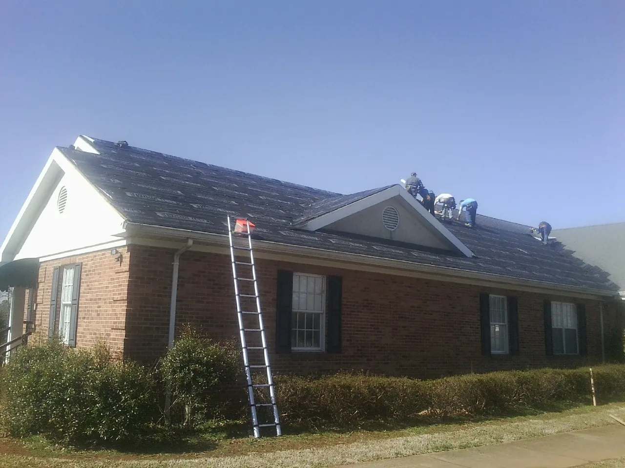 Crew tearing shingles off a brick ranch roof with a ladder set — Emergency Roof Repair work by our crew in Hartville