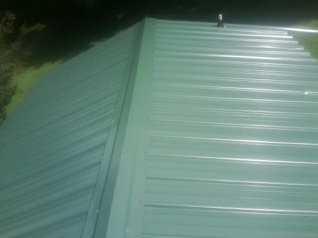 New green metal panels meeting at the ridge of a roof — Flat Roof Repair work by our crew in Hartville