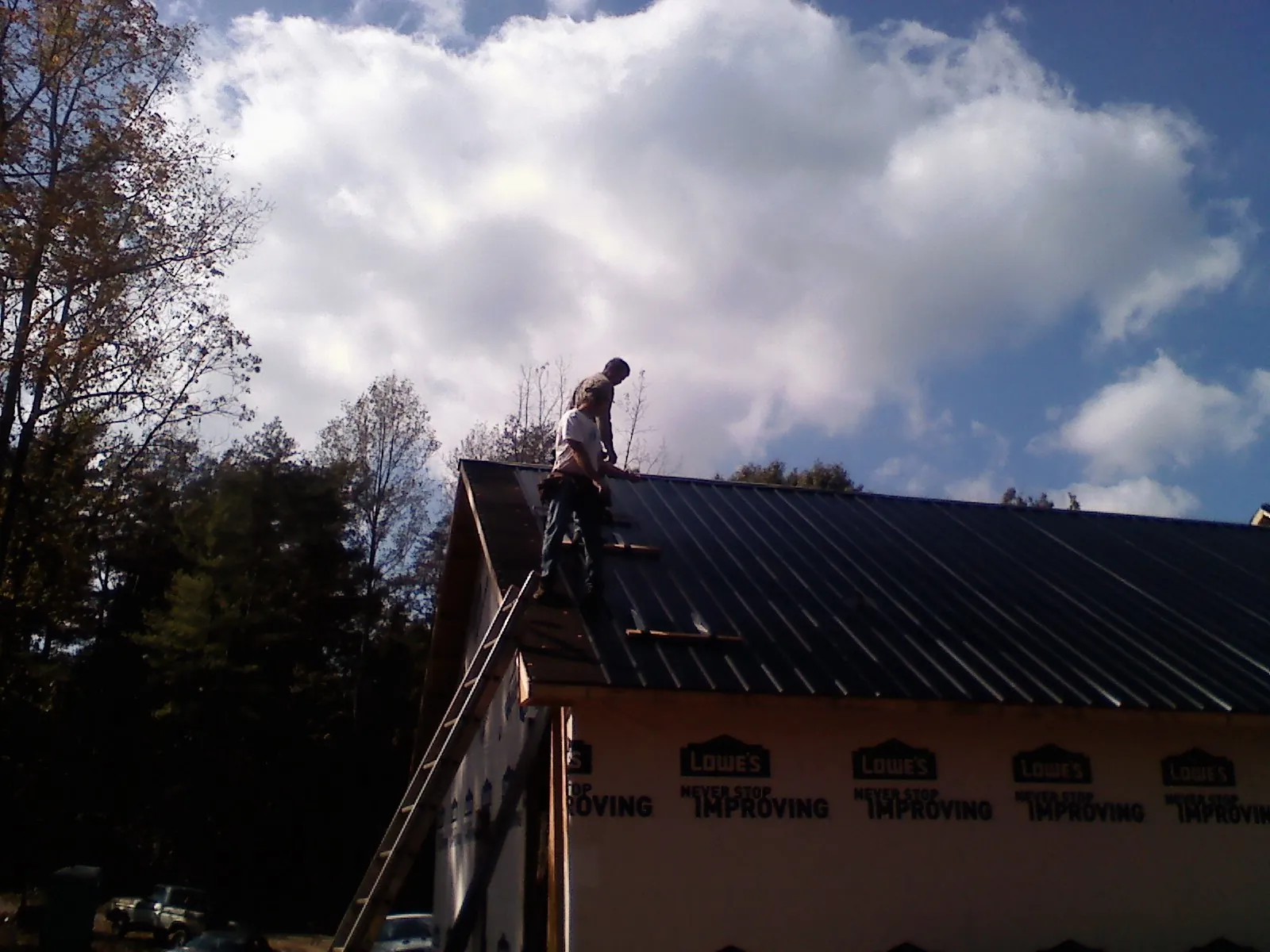 Roofer fastening dark metal panels high against a cloudy sky, from a Roof Inspection job in Hartville
