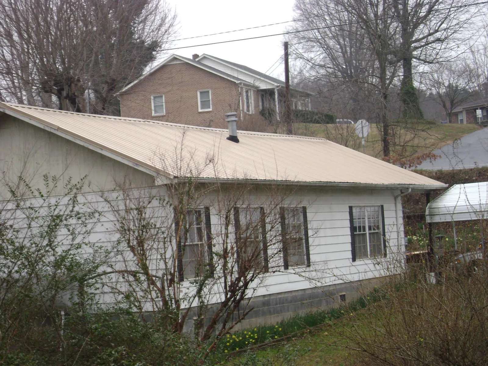 Tan metal roof on a white sided house set into a hillside — Commercial Roofing by Roofing Brothers in Hartville